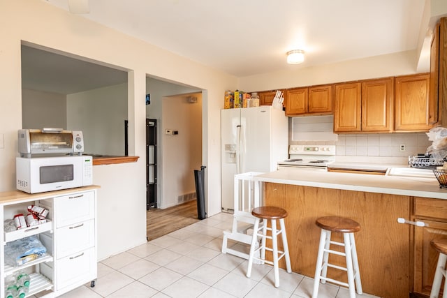 kitchen featuring white appliances, tasteful backsplash, brown cabinets, a breakfast bar, and light countertops