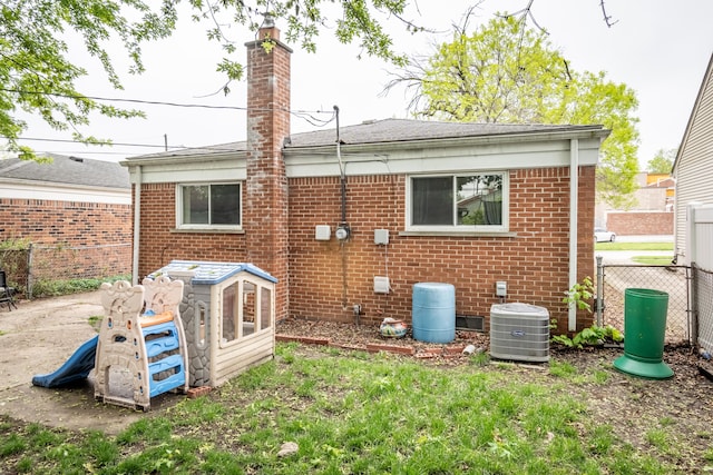 rear view of house with central AC, fence, brick siding, and a chimney
