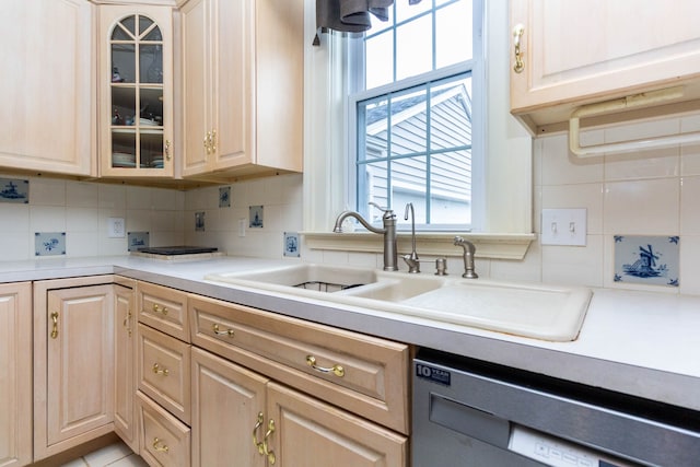 kitchen with stainless steel dishwasher, a sink, backsplash, glass insert cabinets, and light brown cabinetry