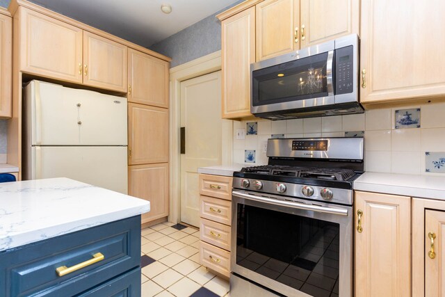 kitchen with stainless steel appliances, light brown cabinets, decorative backsplash, light tile patterned floors, and blue cabinetry