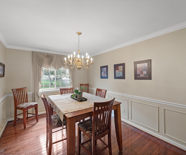 dining space with crown molding, a wainscoted wall, dark wood-style floors, and an inviting chandelier