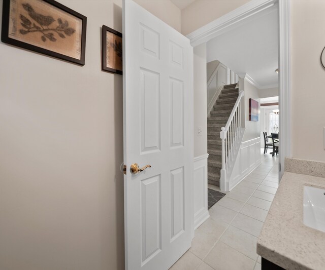 hallway featuring crown molding, stairs, light tile patterned flooring, and a sink