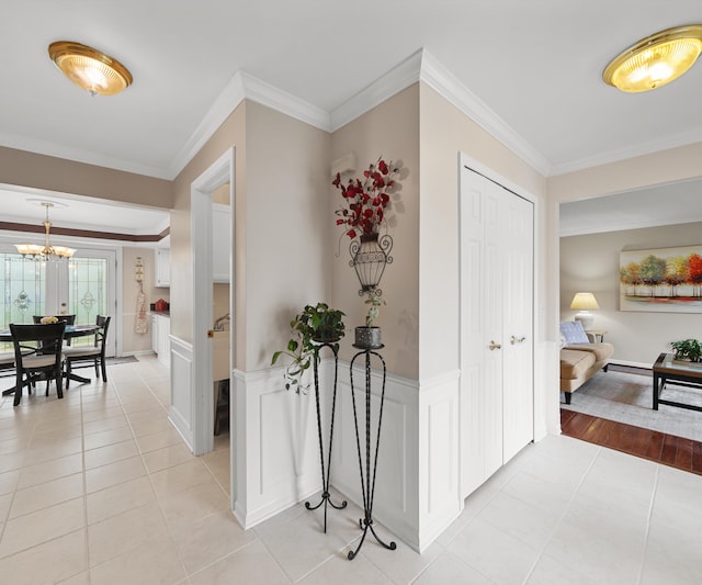 hall featuring crown molding, wainscoting, light tile patterned flooring, and a notable chandelier