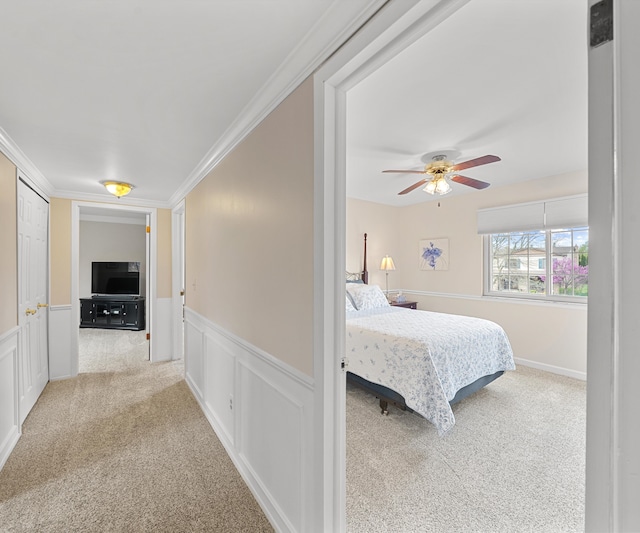 bedroom featuring ornamental molding, carpet, a ceiling fan, and wainscoting