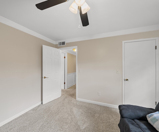 interior space with carpet flooring, a ceiling fan, crown molding, and visible vents
