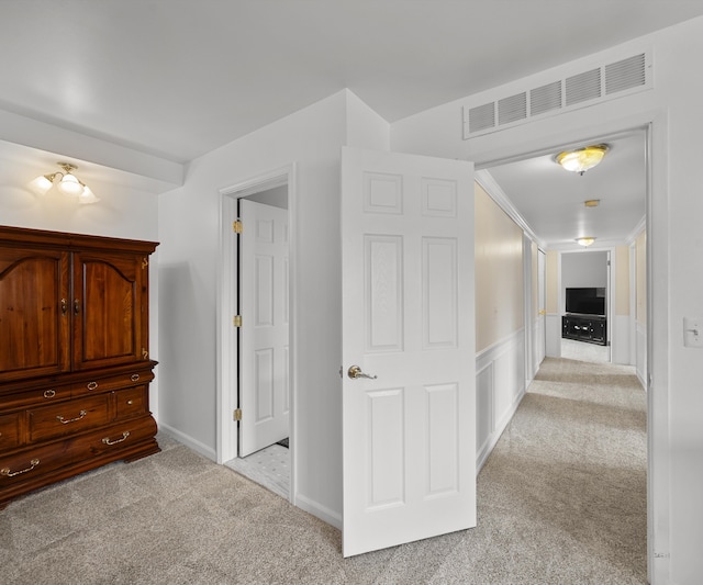 hallway featuring visible vents, wainscoting, and light carpet