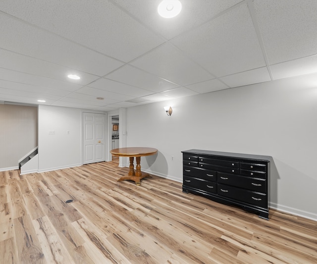 finished below grade area with stairway, baseboards, a drop ceiling, and light wood-style flooring