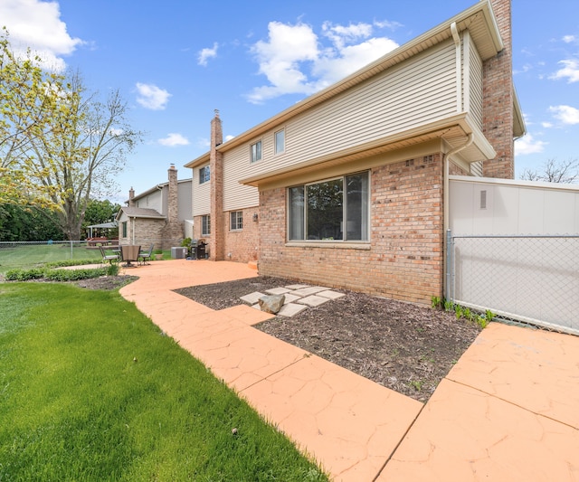 back of property with fence, a chimney, brick siding, a patio area, and a lawn