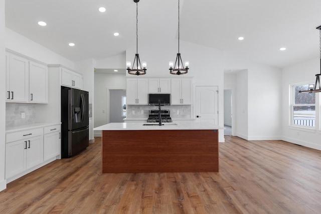 kitchen featuring black refrigerator with ice dispenser, a sink, a chandelier, stainless steel microwave, and vaulted ceiling