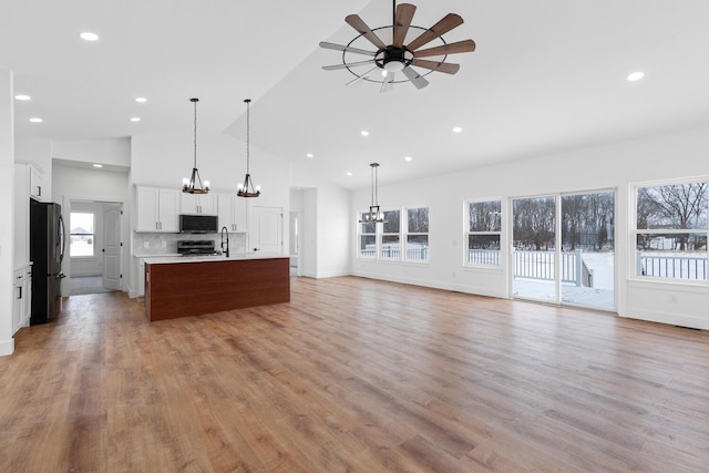 kitchen featuring ceiling fan with notable chandelier, an island with sink, appliances with stainless steel finishes, light countertops, and open floor plan