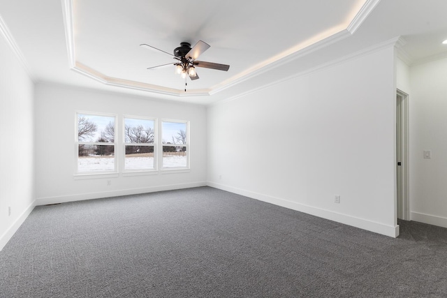 spare room with crown molding, a ceiling fan, a raised ceiling, dark colored carpet, and baseboards