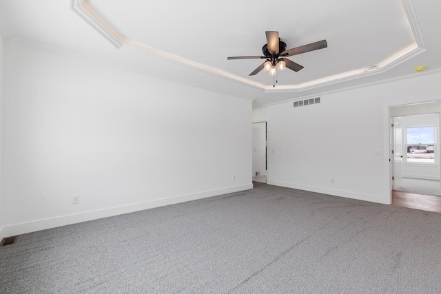 carpeted spare room featuring visible vents, ceiling fan, a raised ceiling, and baseboards