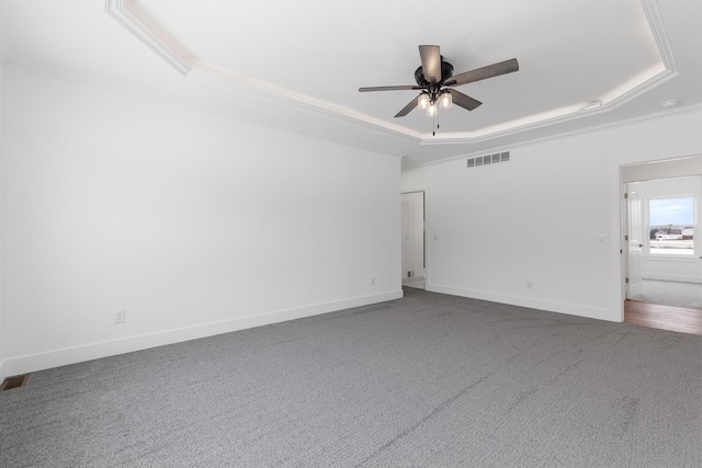 carpeted empty room with visible vents, ceiling fan, a raised ceiling, and baseboards
