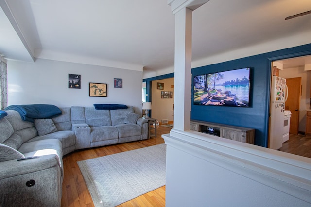 living area featuring wood finished floors, visible vents, ceiling fan, and decorative columns
