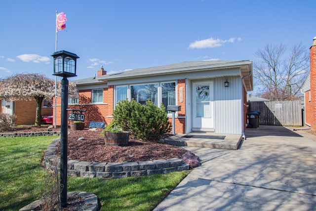 single story home with brick siding, a chimney, concrete driveway, and fence