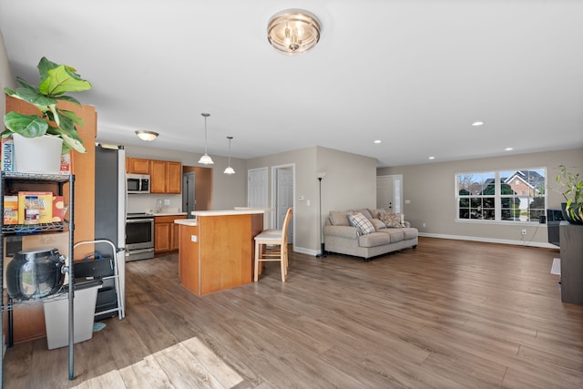 kitchen featuring light countertops, a kitchen breakfast bar, stainless steel appliances, open floor plan, and wood finished floors