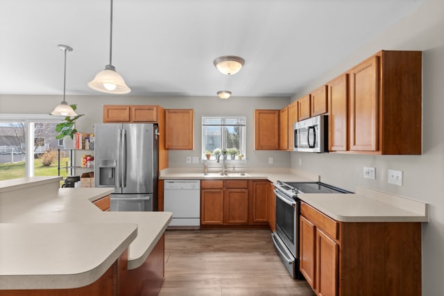 kitchen with light countertops, brown cabinets, a sink, light wood finished floors, and stainless steel appliances