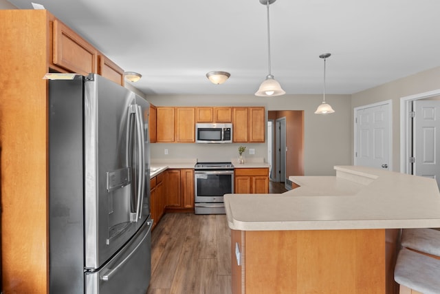 kitchen featuring light countertops, a breakfast bar area, stainless steel appliances, and wood finished floors