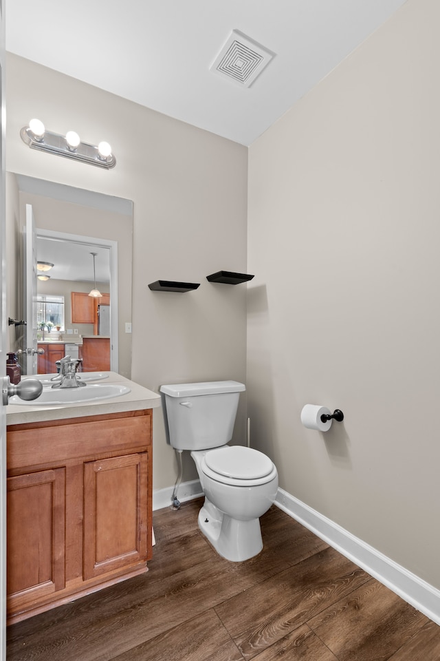 half bathroom with visible vents, wood finished floors, baseboards, vanity, and toilet