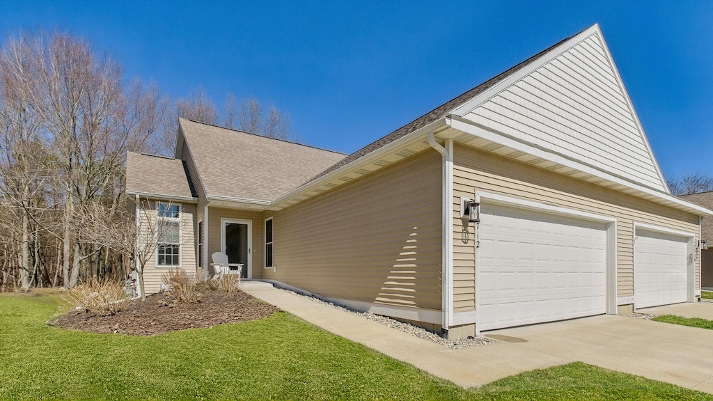 view of property exterior with a shingled roof, an attached garage, driveway, and a lawn