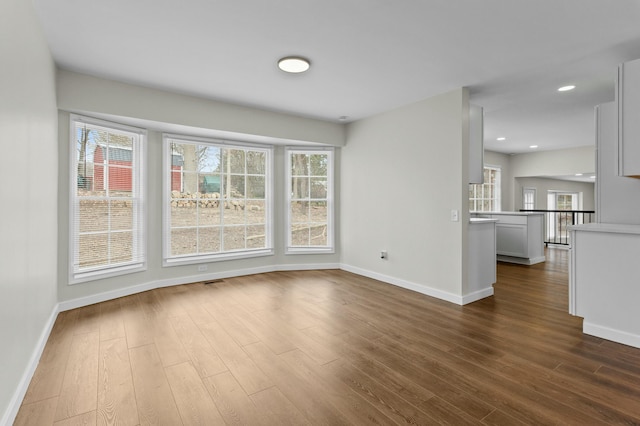 unfurnished living room with recessed lighting, dark wood-type flooring, baseboards, and a healthy amount of sunlight