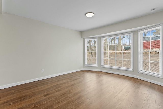 unfurnished room with baseboards, dark wood finished floors, and visible vents