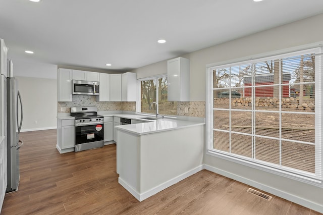 kitchen featuring visible vents, a sink, a peninsula, wood finished floors, and stainless steel appliances