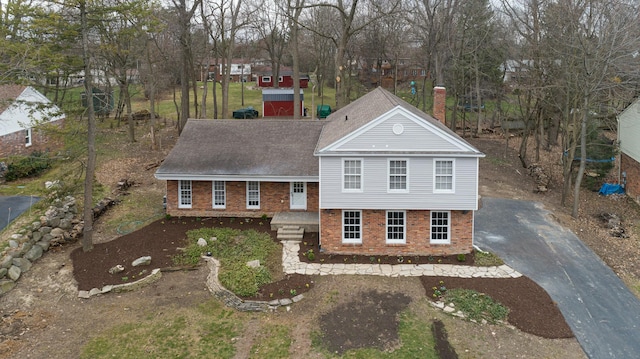 view of front facade featuring brick siding, a shingled roof, driveway, and a chimney