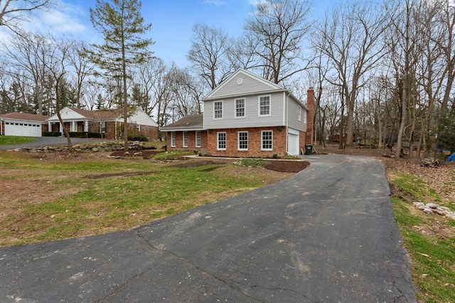 view of front of home with brick siding, aphalt driveway, an attached garage, and a chimney