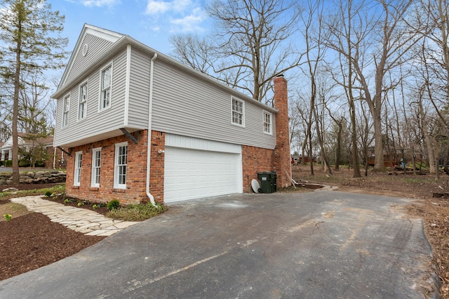 view of property exterior featuring aphalt driveway, brick siding, a chimney, and an attached garage