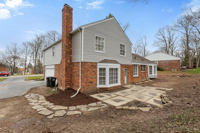 back of house featuring a garage, brick siding, a chimney, and concrete driveway