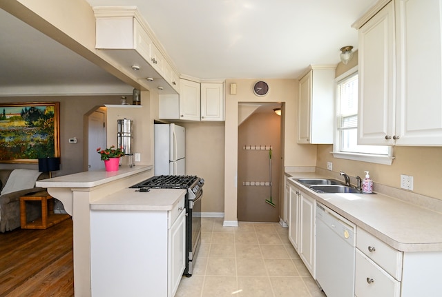 kitchen with white appliances, a sink, light countertops, a peninsula, and baseboards