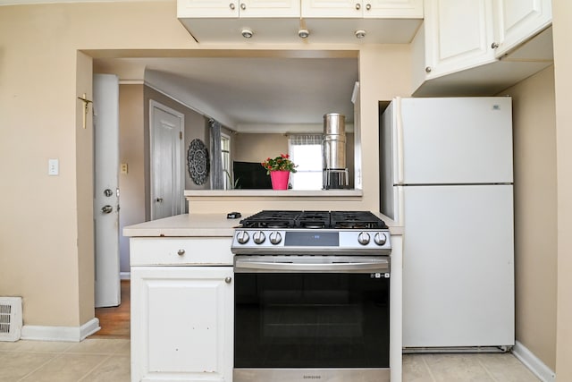kitchen featuring gas range, freestanding refrigerator, light tile patterned floors, white cabinets, and light countertops