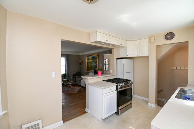 kitchen featuring stainless steel range with gas cooktop, freestanding refrigerator, light countertops, and light tile patterned floors