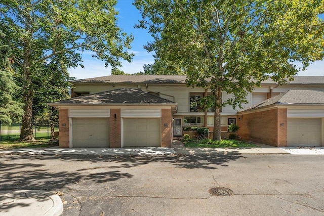 multi unit property featuring brick siding, driveway, a garage, and roof with shingles