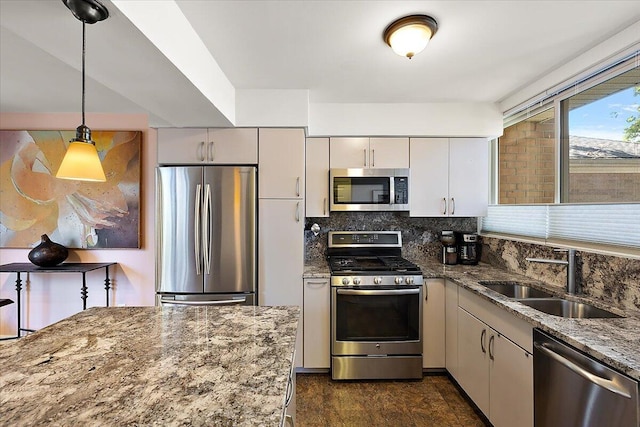 kitchen featuring stone counters, tasteful backsplash, appliances with stainless steel finishes, pendant lighting, and a sink