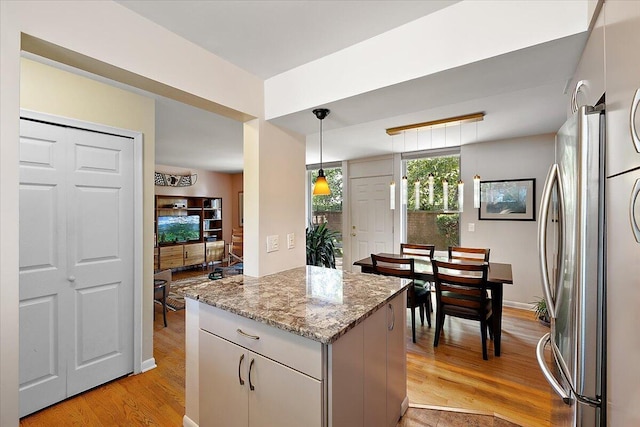 kitchen featuring a center island, light wood-type flooring, freestanding refrigerator, pendant lighting, and light stone counters
