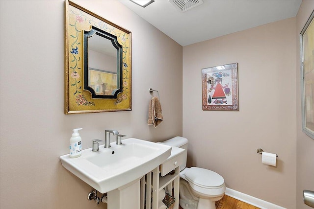 bathroom with baseboards, toilet, visible vents, a sink, and wood finished floors