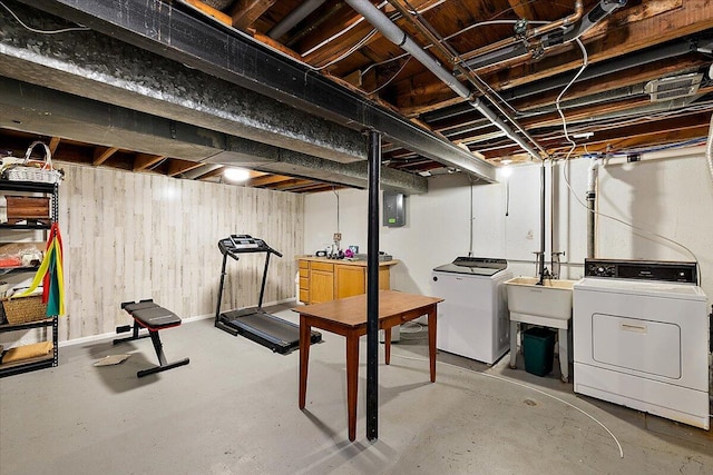 below grade area featuring a sink, wood walls, washing machine and dryer, and electric panel