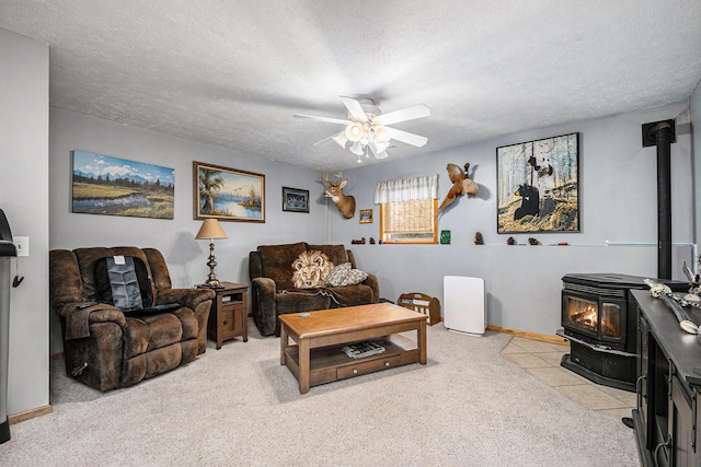 living room with a textured ceiling, a wood stove, baseboards, light carpet, and a ceiling fan