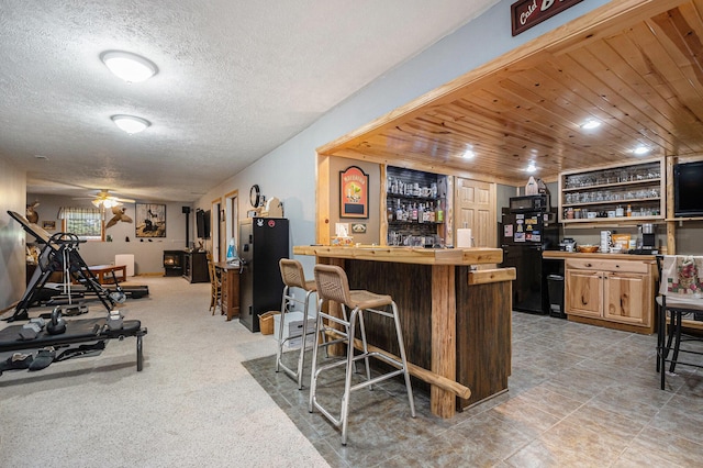 bar featuring a textured ceiling, ceiling fan, a bar, and freestanding refrigerator