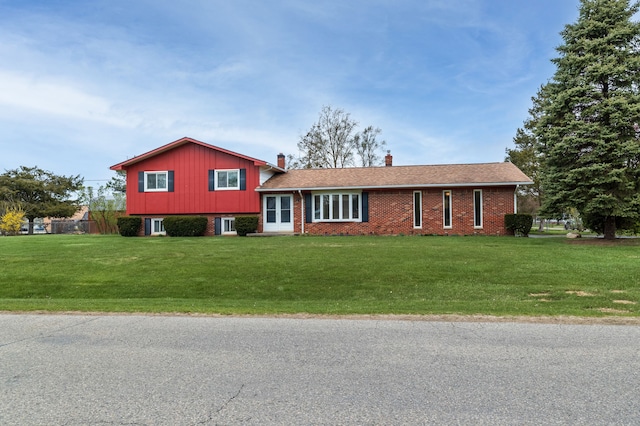 split level home with a front yard, a chimney, and brick siding