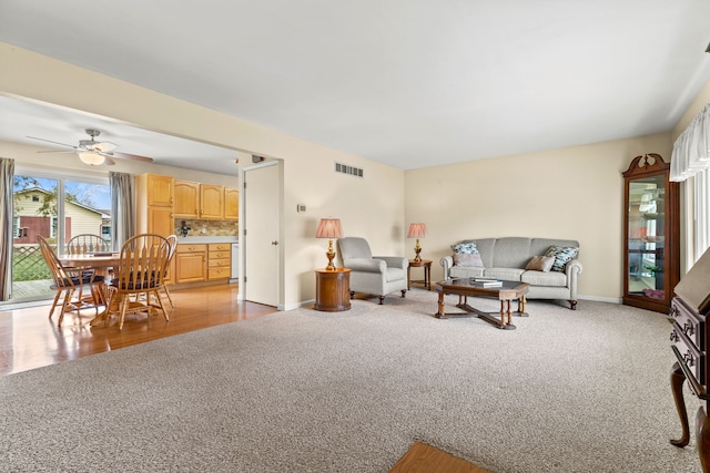 living area featuring baseboards, visible vents, ceiling fan, and light colored carpet