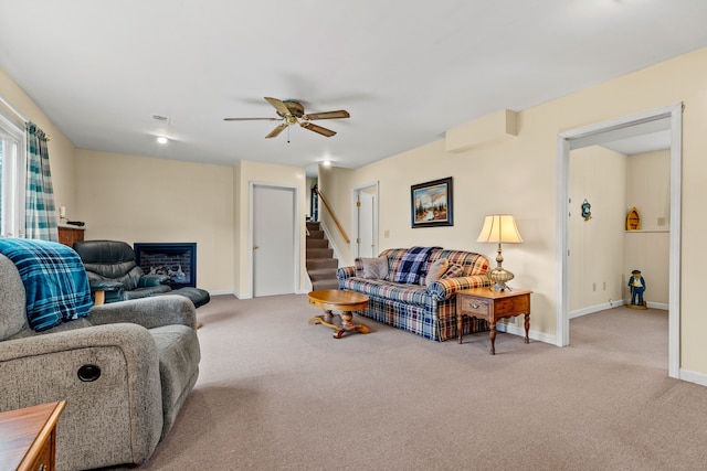 living area featuring carpet flooring, stairway, a ceiling fan, visible vents, and baseboards