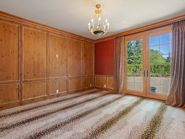 unfurnished room with a decorative wall, ornamental molding, carpet flooring, a notable chandelier, and french doors