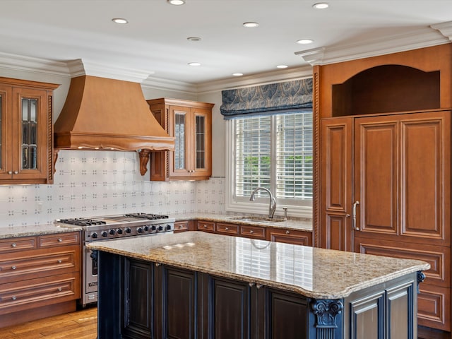 kitchen featuring light stone counters, high end stainless steel range oven, a sink, a kitchen island, and custom exhaust hood