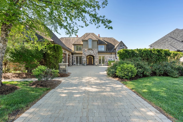 view of front facade with decorative driveway, a front yard, french doors, and stone siding