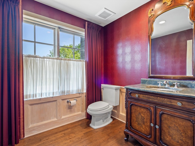 half bathroom with toilet, vanity, visible vents, and wood finished floors