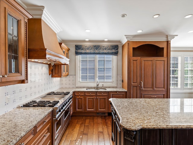 kitchen featuring hardwood / wood-style flooring, light stone counters, double oven range, and a sink
