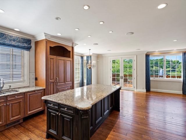 kitchen with a sink, a chandelier, crown molding, light stone counters, and a kitchen island
